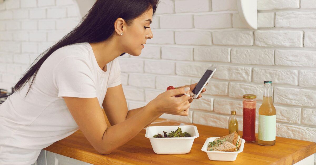 Woman photographing her meal on her phone at a kitchen counter to track what she eats