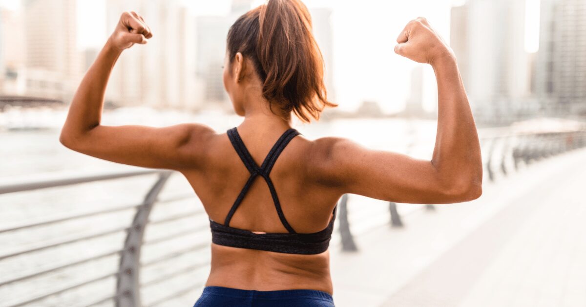 Woman in workout clothes flexing both arms, seen from behind