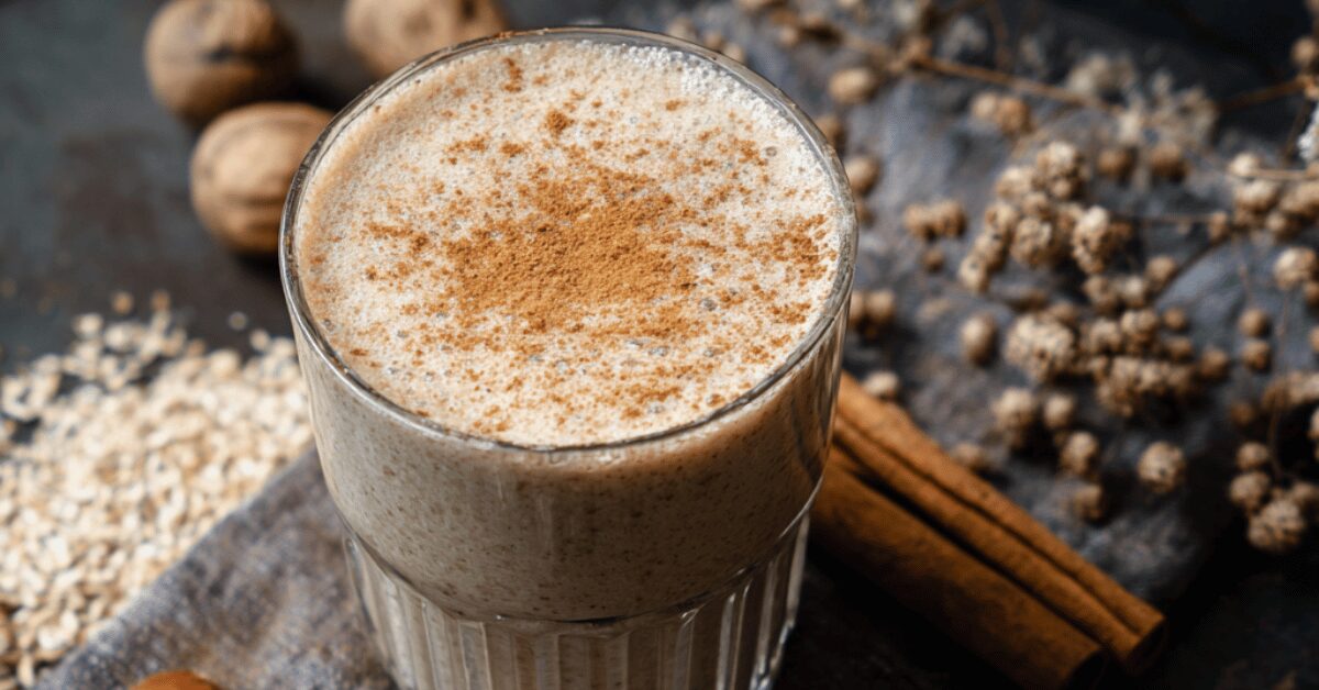 Creamy gingerbread protein smoothie in a glass, dusted with cinnamon, with cinnamon sticks and walnuts