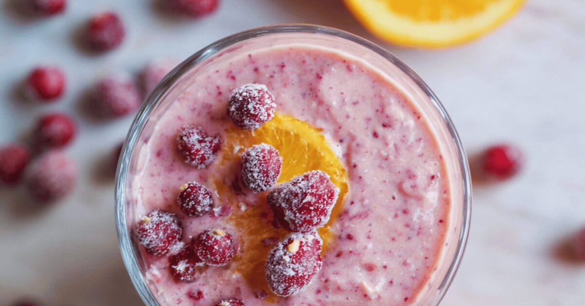 Pink cranberry orange smoothie topped with frosted cranberries and an orange slice