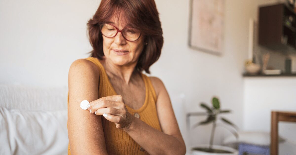 Woman in glasses applying a small round hormone patch to her skin