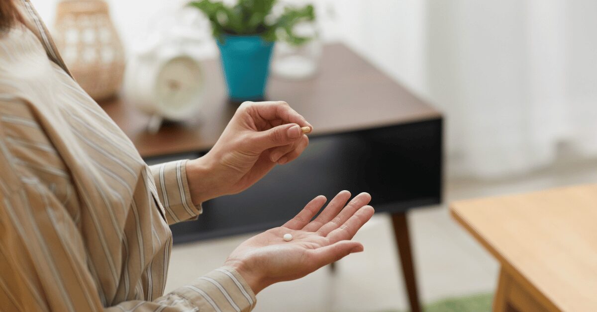 Woman holding a small pill between her fingertips over her open palm