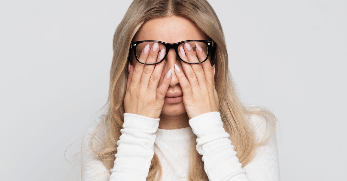 Tired woman in glasses rubbing her eyes with both hands