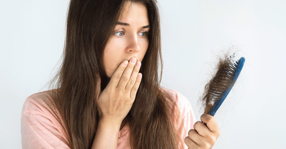 Woman looking with surprise at a hairbrush full of shed hair