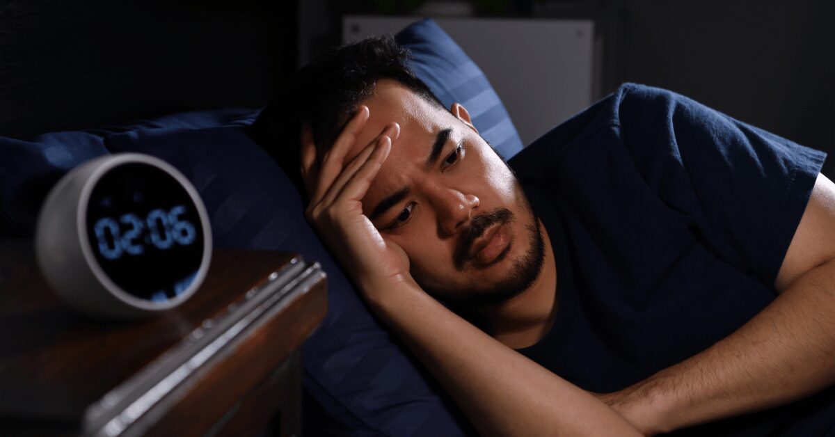 Man lying awake in bed at night next to a clock reading 2:06