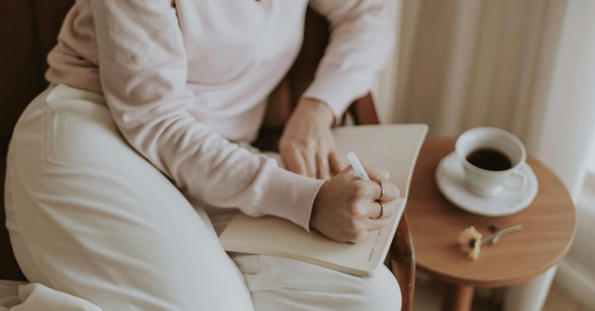 Woman writing in a notebook beside a cup of coffee