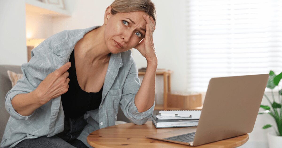Tired, overheated woman at her laptop with a hand on her forehead