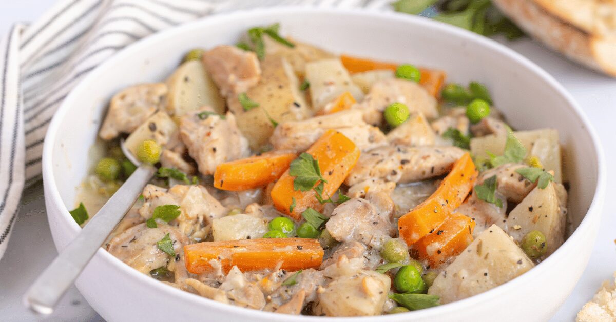 Bowl of creamy chicken stew with carrots, potatoes, and green peas